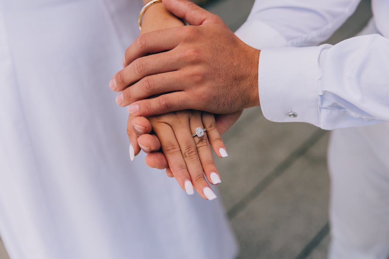 Close-up of a couple holding hands, showcasing an elegant diamond engagement ring.